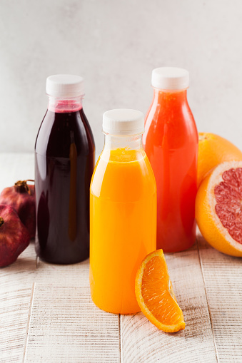 Freshly squeezed orange, grapefruit, pomegranate juices in transparent bottles on a light wooden background. The concept of healthy nutrition, detox.