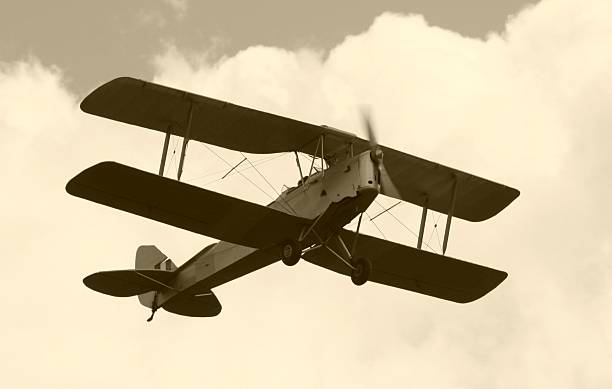 Black and white photo of Tiger Moth flying through clouds Tiger Moth in Sepia. world war i photos stock pictures, royalty-free photos & images