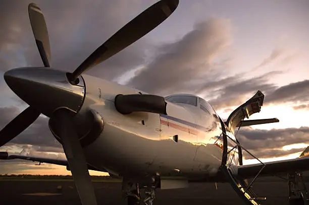 A PC12 single engine aircraft viewed from the front and down low during sunset lighting.Click