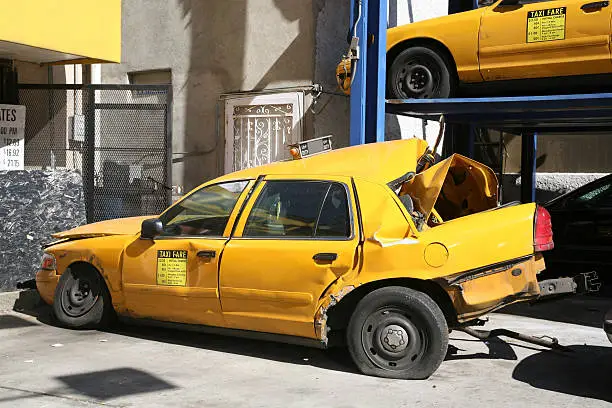 Damaged taxicab with crushed rear end parked outside an auto repair shop, New York City, New York, USA.