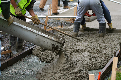 Construction workers pour and smooth concrete on a sidewalk renewal project.