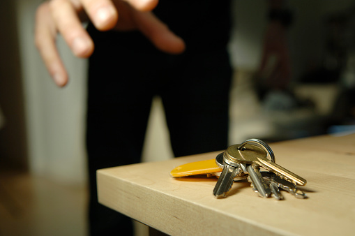keys on wooden table with figure reaching out grabbing hand - very shallow depth of field