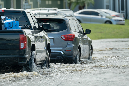 Hurricahe rainfall flooded Florida road with evacuating cars and surrounded with water houses in suburban residential area.