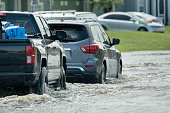 Hurricahe rainfall flooded Florida road with evacuating cars and surrounded with water houses in suburban residential area