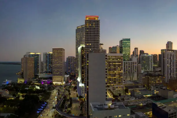 Aerial view of downtown district of of Miami Brickell in Florida, USA. Brightly illuminated high skyscraper buildings and street with cars and Metrorail traffic in modern american midtown.