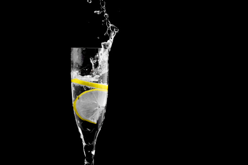 Big Splash of drink fluid in a glass with two peaces of lemon on black background