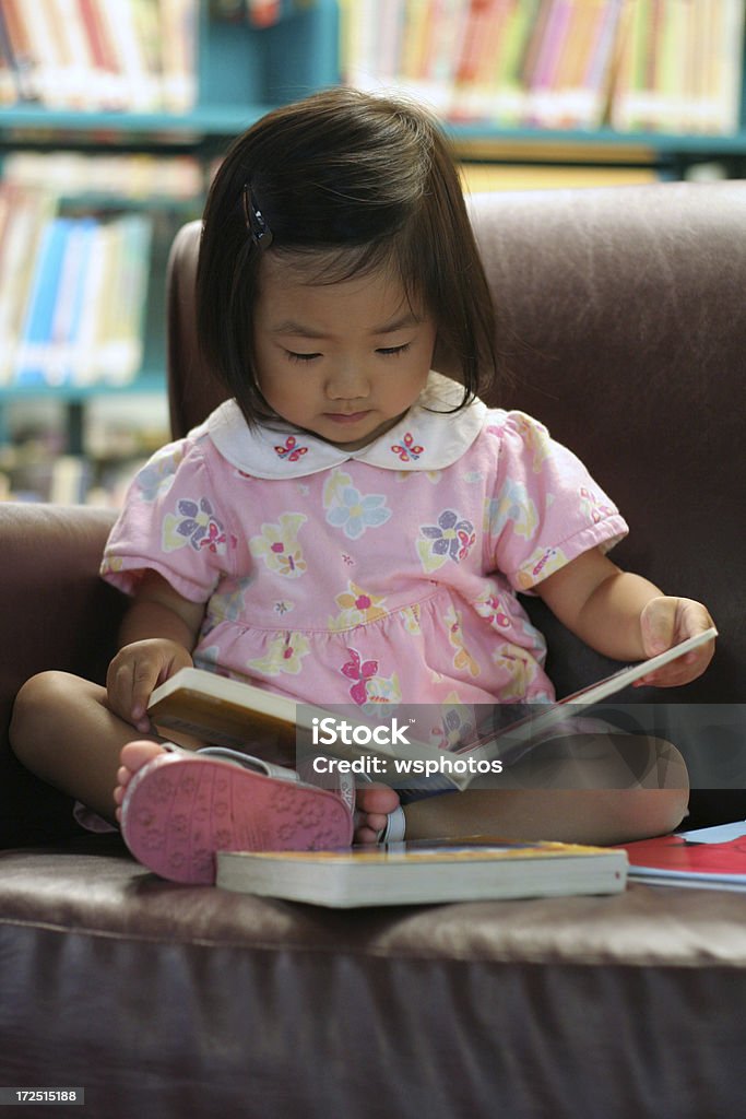 Carino piccolo ragazza asiatica leggendo un libro in biblioteca preschool - Foto stock royalty-free di 2-3 anni