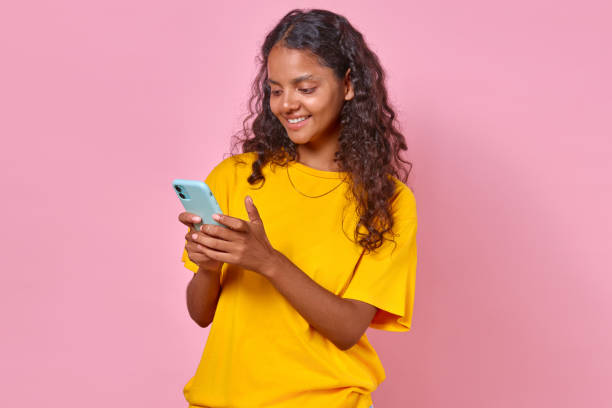 istock Young cheerful Indian woman holding phone using mobile apps stands in studio 1725174072