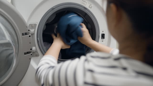 Asian woman putting clothes into the washing machine