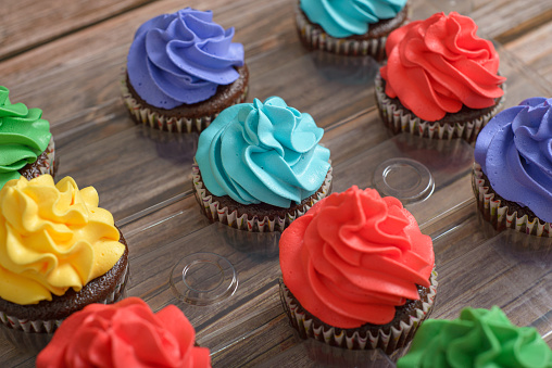Multicolored cupcakes on wooden table. Colorful desserts.