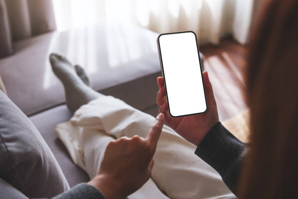 istock Mockup image of a woman holding mobile phone with blank desktop white screen while lying on a sofa at home 1725355701