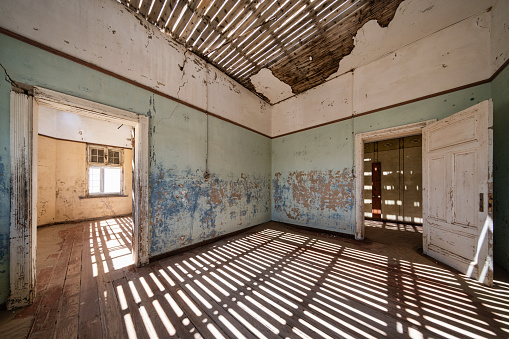 Namibia Lüderitz Ghost Town Building Interior. Old rotting domestic room inside abandoned Ghost Town Building with sunlight and shadow Textures reflecting from the open roof and window. Old Diamond Mining Building of abandoned Kolmanskop Diamond Mine, Lüderitz, Namibia, Africa