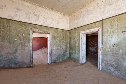 Namibia Old Diamond Mining Ghost Town Barrack Interior. Nature is coming back. Desert Sand - Sand Dune entering an old abandoned german colonial house ínside deserted Diamond Mine Ghost Town close to Kolmanskop, Luderitz - Lüderitz, Namibia, Africa.