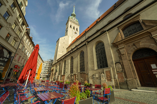 Munich, Germany, Bavaria, Europe - September 18, 2023. St. Peter's Church view from a city street with a colorful outdoor restaurant, located in the city center right next to Marienplatz and Viktualienmarkt. Dating back to the 12th century, St Peter's Church, or Peterskirche, is Munich's oldest church and one of the most important symbols of the city.