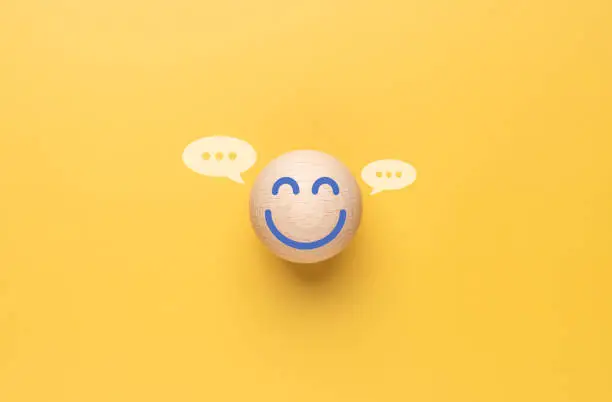 Photo of Happy smiley face emotion on the wooden circle with the yellow background. Customer service evaluation, Positive thinking and mental health assessment. Satisfied customer giving feedback with delight.