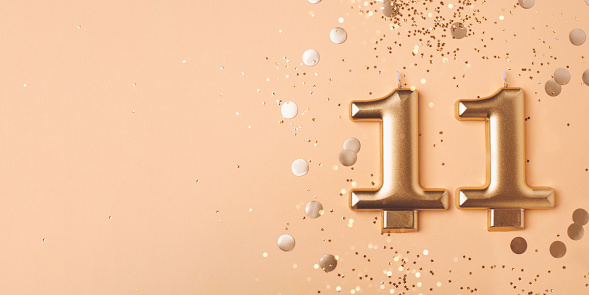 Gold candles in the form of number eleven on peach background with confetti. 11 years celebration.