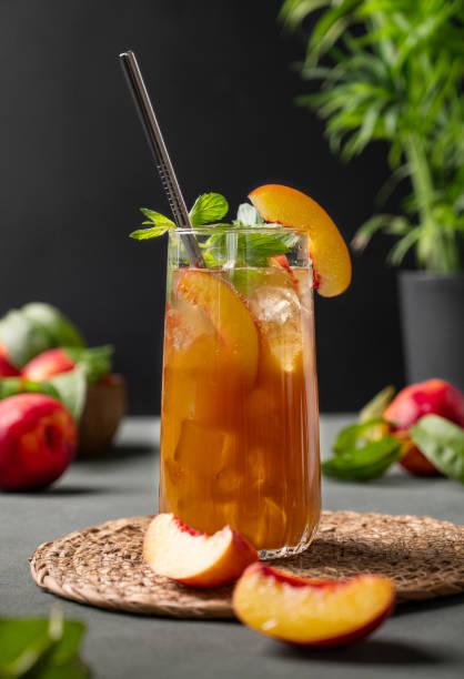 thé à la pêche avec de la glace et de la menthe sur un grand verre. boisson estivale froide maison végétalienne sur fond sombre avec des fruits frais. - georgia peach photos et images de collection