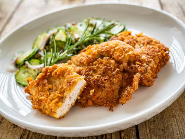 istock Breaded seared chicken cutlets with fresh vegetable salad on wooden table 1725497358
