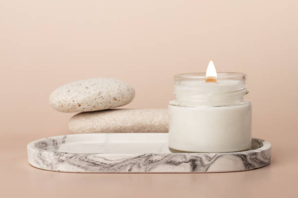 istock Handmade burning candle on a marble tray with pebble stones on a beige background 1725513377