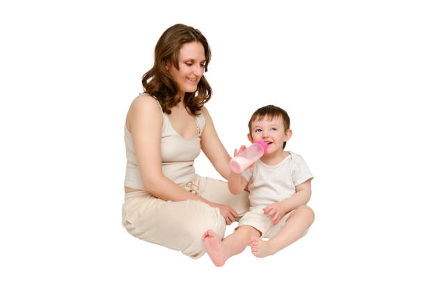 istock Happy baby with mother drinks milk from bottle on studio, isolated on white background. Resting child with mom eats formula, isolated white background. Kid about two years old (one year nine months) 1725516187