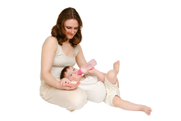 istock Happy baby with mother drinks milk from bottle on studio, isolated white background. Resting child with mom eats formula, isolated on white background. Kid about two years old (one year nine months) 1725516191
