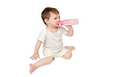 Happy baby drinks milk from bottle on studio, isolated on white background. Resting child eats formula, isolated on white background. Kid about two years old (one year nine months)
