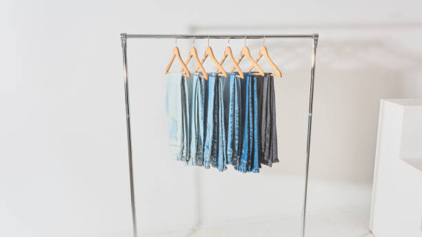 mobile clothes hanger. clothes rail with jeans of different colors hanging on hangers light minimalistic studio with a mobile clothes hanger. clothes rail with jeans of different colors hanging on hangers clothes hanger rod stock pictures, royalty-free photos & images