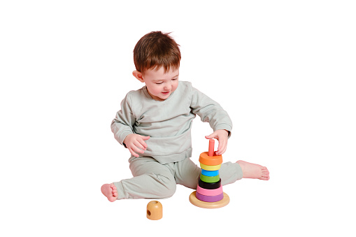 Happy toddler baby plays with a pyramid on a studio, isolated on white background. Child boy puts wooden rings on a toy pyramid, isolated on white background. Kid age one year eight months