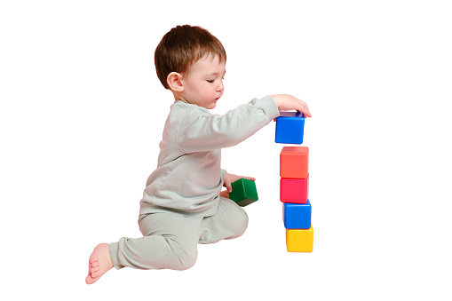 Happy toddler baby plays with cubes on studio, isolated on white background. Child boy builds a tower of toys, isolated on white background. Kid age one year eight months, full height