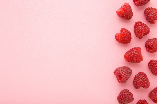 Fresh red raspberries on light pink table background. Pastel color. Closeup. Top down view. Empty place for text.