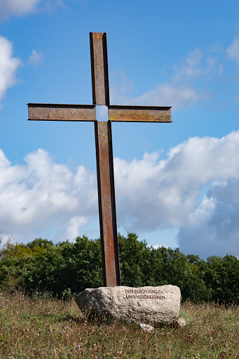 A view of an old historic cemetery located in the middle of a well maintained field or meadow, with stone and wooden crosses, marble blocks, and some benches seen next to a well maintained path