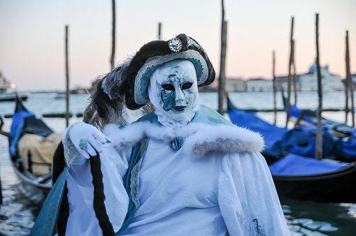 Venice, VE, Italy - February 13, 2024: masquerade woman with luxurious dress of white and blue color  and a gondola