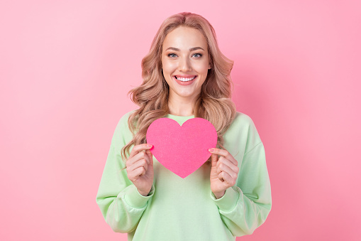 Photo of cheerful young blonde hair girlfriend holding paper postcard happy valentine day celebration isolated on pink color background.