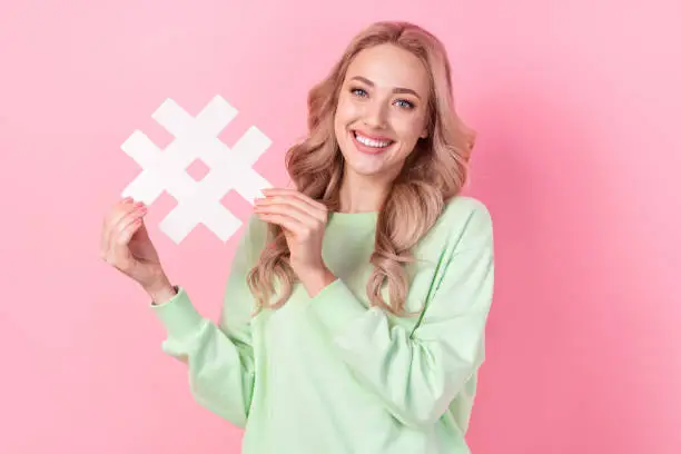 Photo of Photo of popular blogging young girl influencer holding paper hashtag symbol follow channel trend video isolated on pink color background