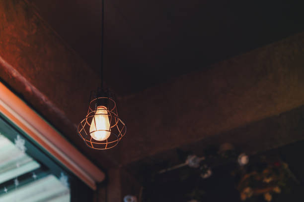 istock A vintage style light bulb with a metal frame around it hangs from the ceiling, glowing with a golden yellow glow. Home decoration ideas. 1725591648