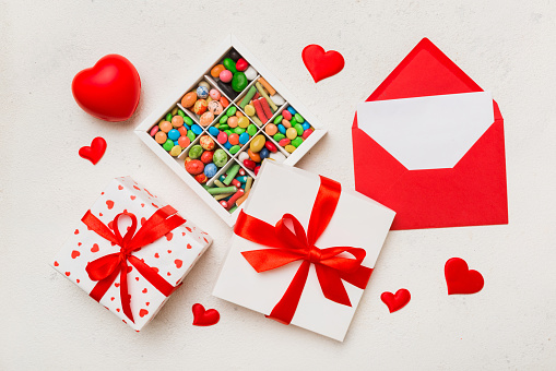 Red envelope with candy and gift box and Valentines hearts on colored background. Flat lay, top view. Romantic love letter for Holiday concept.