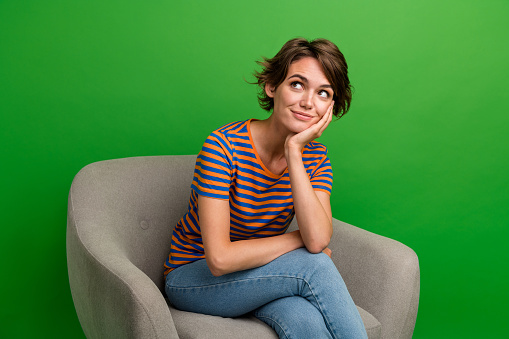 Photo of gorgeous minded lady sit cozzy chair arm touch cheek look empty space isolated on green color background.
