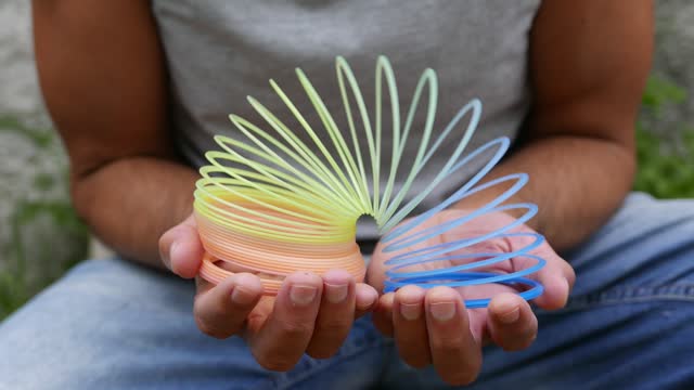 Colorful toys: a rainbow coil spring. A person playing with a slinky. Person playing with a spiral toy. Person playing with a colorful slinky. Rainbow spring slinky. Plastic colorful spring. Plastic coil spring toy