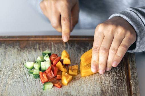 A woman cuts vegetables on a cutting board for salad, close-up.