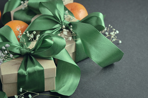 Paper gift boxes with green ribbons tied in a bow, tangerines, black background. Decoration for holidays, birthdays, weddings.