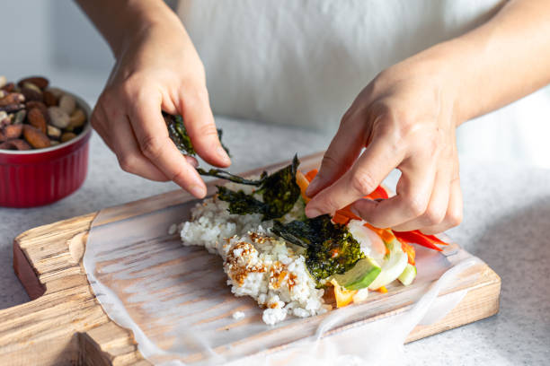 istock Woman preparing spring rolls in rice paper on kitchen table. 1725654583