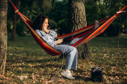 A woman in a hammock in nature works on a laptop charging from a portable charging station