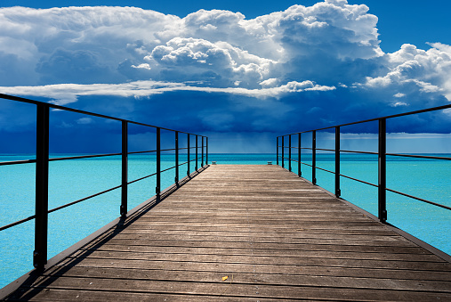 Close-up of a wooden pier (diminishing perspective) against a beautiful turquoise seascape and sky with storm clouds (cumulonimbus) and torrential rain.