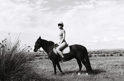 A young woman rides a horse across a plain, 35mm black and white film, Devon UK.