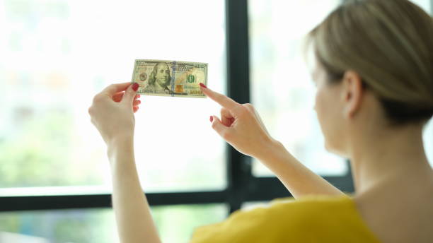 фальшивый денежный чек. 100 долларов против окна в рук�е - деньги окно стоковые фото и изображения