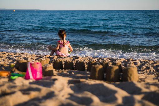 The child is sitting on the seashore and playing with the sea waves. The child is using the plastic toys to play with water and sand.