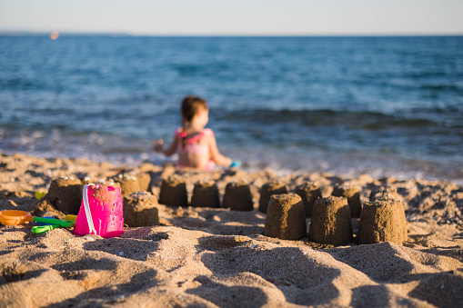 A three-year-old girl made a sandcastle on the seashore. The little girl left her sandcastle and toys and went to the sea to play with the water.