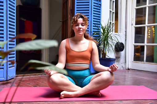 Mid adult woman meditating in lotus position at yoga studio