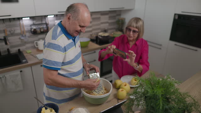 Senior couple making an apple pie in modern kitchen