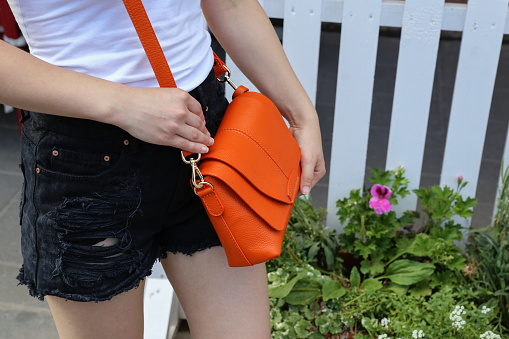 A girl in a white T-shirt and torn brutal black shorts with a bright orange leather bag. A casual, fashionable look in a minimalist style.